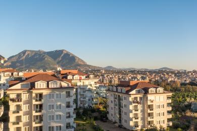Σύγχρονο διαμέρισμα σε συγκρότημα στην Αλάνια με θέα στο βουνό, μοντέρνα αρχιτεκτονική και ζεστή, ηλιόλουστη ατμόσφαιρα.